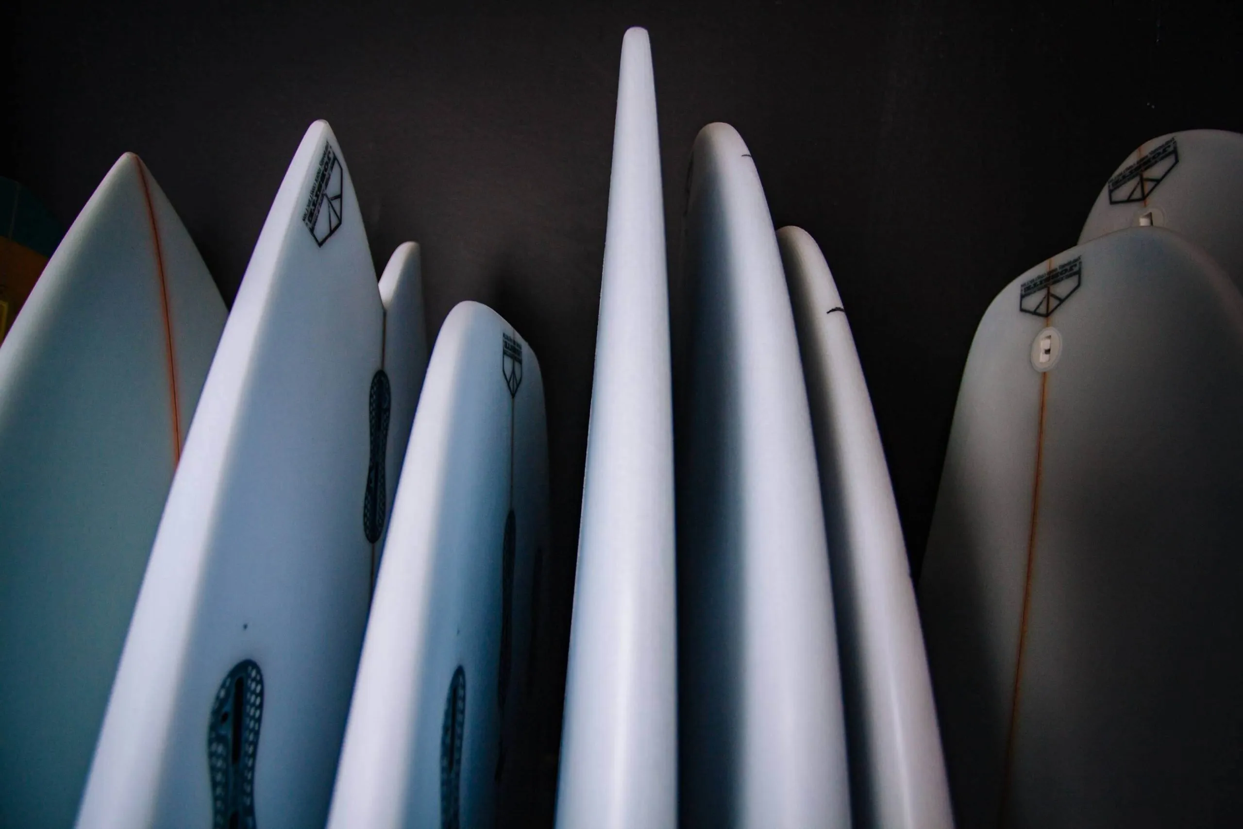 Close-up of multiple white surfboards with logos from various brands