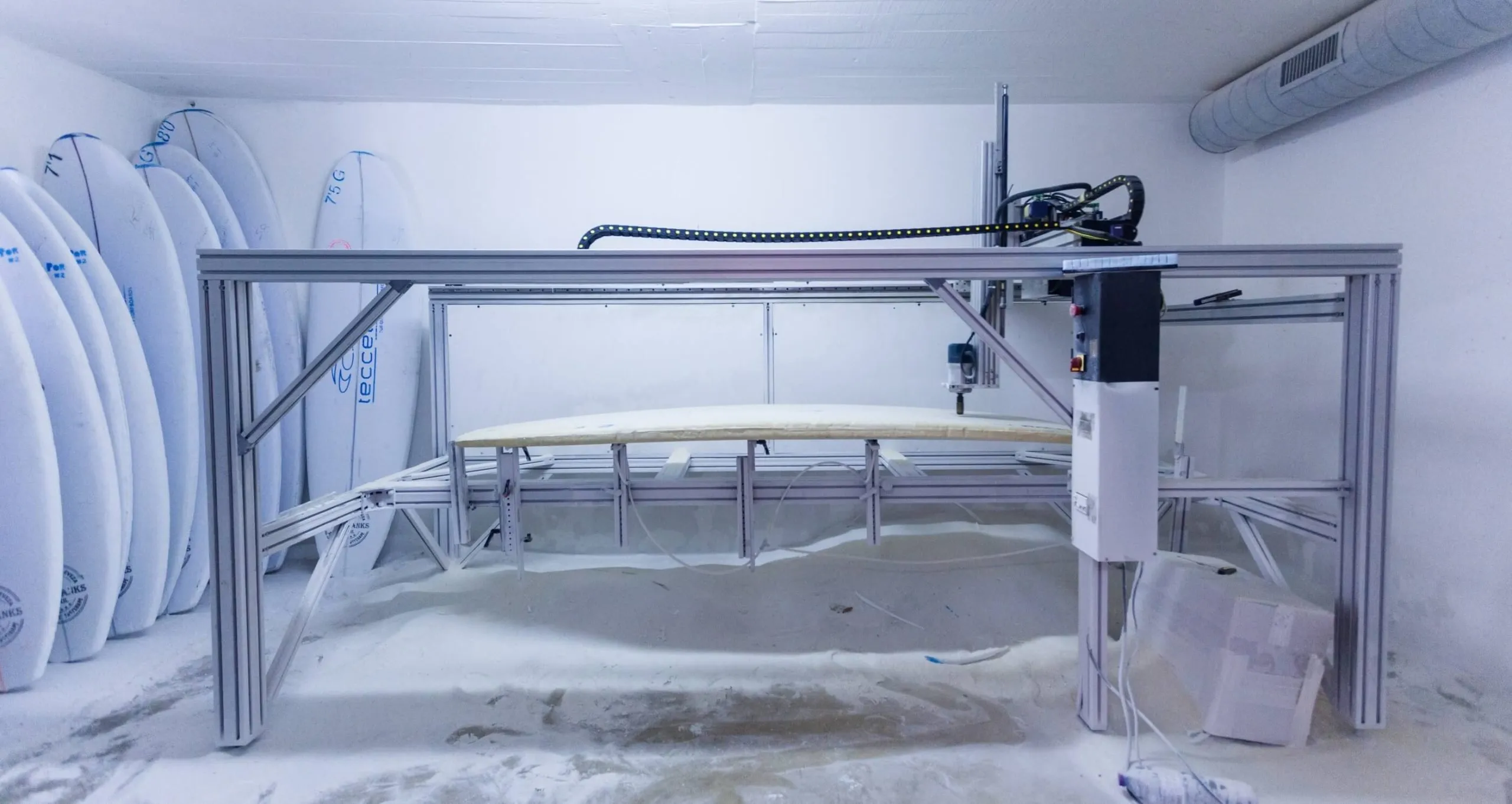 CNC machine cutting a surfboard in a workshop with surfboards on the wall